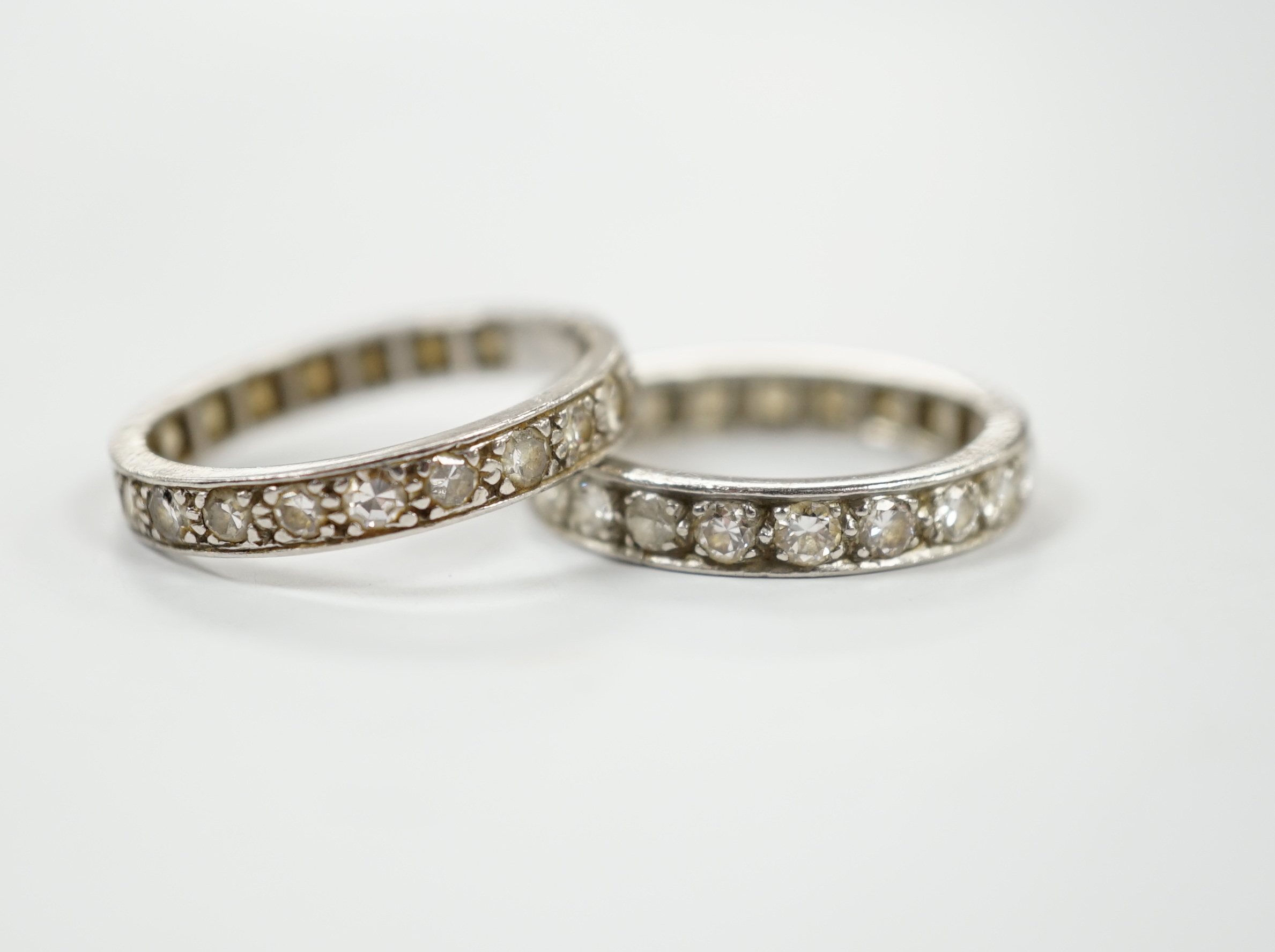 Two white metal and diamond set full eternity rings, one with cut shank and stone missing, sizes L & P, gross weight 7.7 grams.